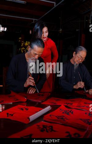 Fille vietnamienne avec la robe rouge Ao Dai et de vieux érudits écrivant calligraphie au nouvel an lunaire. La calligraphie est une tradition populaire pendant les vacances du Têt. T Banque D'Images