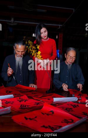 Fille vietnamienne avec la robe rouge Ao Dai et de vieux érudits écrivant calligraphie au nouvel an lunaire. La calligraphie est une tradition populaire pendant les vacances du Têt. T Banque D'Images