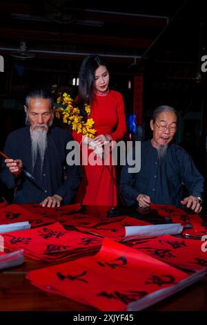 Fille vietnamienne avec la robe rouge Ao Dai et de vieux érudits écrivant calligraphie au nouvel an lunaire. La calligraphie est une tradition populaire pendant les vacances du Têt. T Banque D'Images