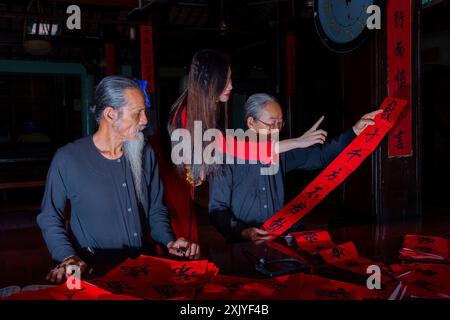 Fille vietnamienne avec la robe rouge Ao Dai et de vieux érudits écrivant calligraphie au nouvel an lunaire. La calligraphie est une tradition populaire pendant les vacances du Têt. T Banque D'Images