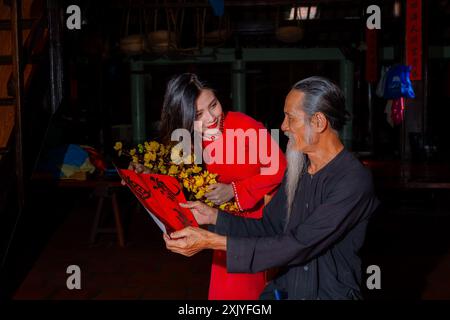 Fille vietnamienne avec la robe rouge Ao Dai et de vieux érudits écrivant calligraphie au nouvel an lunaire. La calligraphie est une tradition populaire pendant les vacances du Têt. T Banque D'Images