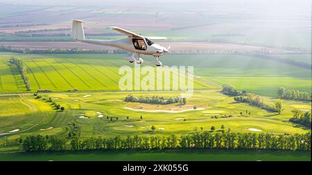 L'avion à moteur léger vole dans les nuages du ciel du matin à l'aube au-dessus des champs Banque D'Images