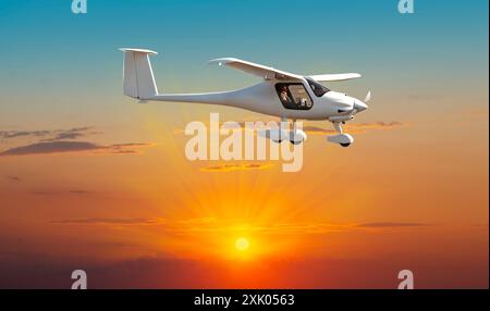 L'avion à moteur léger vole dans le lever du soleil avec une doublure argentée et des nuages sur le ciel orange Banque D'Images