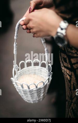 Une femme dans une robe noire tient un petit panier en osier blanc avec une poignée blanche. Banque D'Images