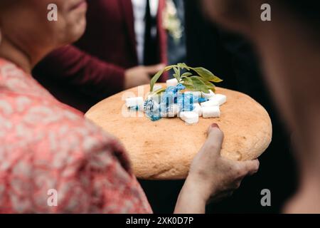 Une femme tient une miche ronde de pain ornée de petits cubes blancs, de bonbons bleus et d'une branche de menthe. Banque D'Images