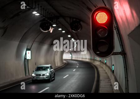 Une voiture blanche traverse un tunnel avec un feu rouge suspendu au plafond. Banque D'Images