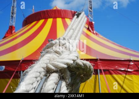 Bridgend, pays de Galles - 7 juillet 2024 : Grande tente de cirque jaune et rouge. Cordes épaisses solides nouées et attachées sur des cliquets métalliques pour assurer la sécurité. Banque D'Images