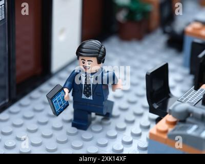 Tambov, Fédération de Russie - 19 juillet 2024 Un homme d'affaires Lego minifigure marchant dans un bureau et tenant un téléphone portable. Banque D'Images