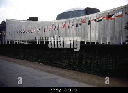 New York, États-Unis. Septembre 1959 : vue du siège de l'Organisation des Nations Unies (ONU) dans le quartier Turtle Bay de Midtown Manhattan à New York. Achevé en 1952, le complexe a été conçu par un conseil d'architectes dirigé par Wallace Harrison et construit par le cabinet d'architectes Harrison & Abramovitz. Devant le bâtiment se trouve une rangée de drapeaux représentant les états membres des Nations Unies. Banque D'Images