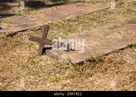 Goiania, Goias, Brésil – 20 juillet 2024 : une croix de ciment couchée dans la tombe sur le sol. Détail d'un cimetière. Banque D'Images