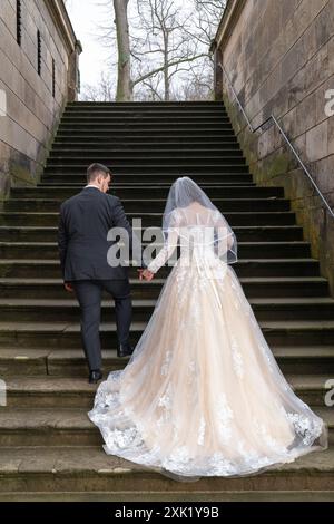 La mariée et le marié marchent le long des marches de pierre d'un ancien bâtiment, un palais. Vue arrière, depuis l'arrière. La mariée porte un beau lon Banque D'Images