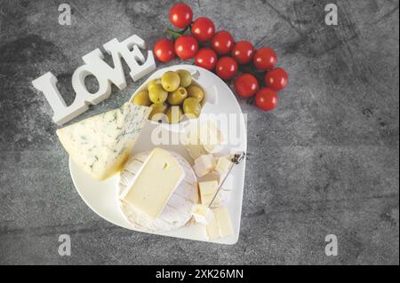 Délicieux fromages à moisissure blanche avec des olives sur un plateau de fromage original en forme de cœur. Un assortiment de fromages avec des moisissures blanches et bleues sur la table Banque D'Images