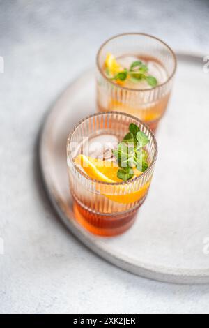 Deux élégants verres remplis d'un cocktail estival vibrant composé de liqueur de cerise et de tonique, garnis d'une tranche fraîche de feuilles d'orange et de menthe, Banque D'Images