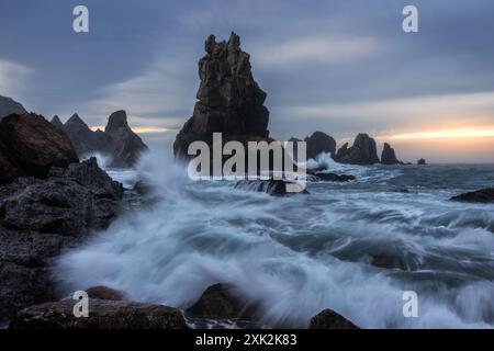 Les vagues dynamiques s'écrasent contre les falaises accidentées de la Costa Quebrada en Cantabrie, en Espagne, sous un ciel doux au lever du soleil Banque D'Images