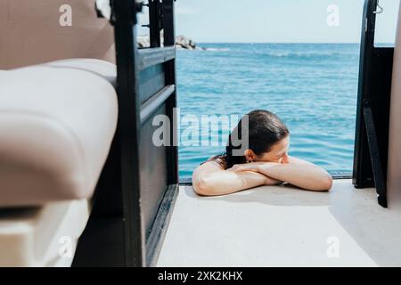 Cette image capture un moment serein d'une femme se relaxant au bord de la mer pendant les vacances d'été, on la voit reposer sa tête sur ses bras, profitant de la paix Banque D'Images