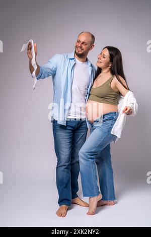 Une femme enceinte dans une chemise blanche, un Jean bleu avec le ventre exposé et son mari tiennent une photo de leur nouveau-né à naître. Grossesse, mites Banque D'Images