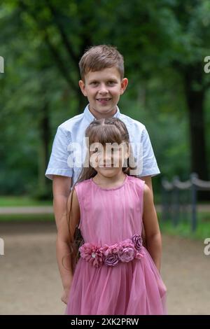 Portrait de frère et sœur. Un garçon de 10 ans embrasse sa sœur cadette de 6 ans. La fille est habillée d'une belle robe rose Banque D'Images