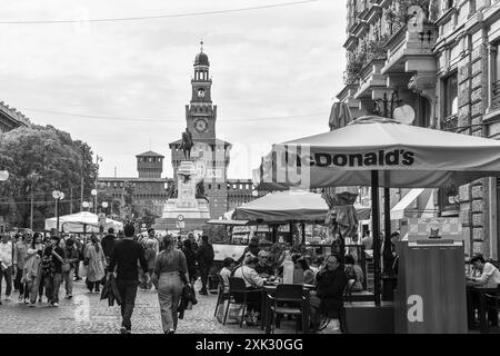 N&B Les gens déjeunent dans un restaurant de restauration rapide McDonald's avec le monument à Giuseppe Garibaldi et le Castello Sforzesco, Milan, Italie Banque D'Images