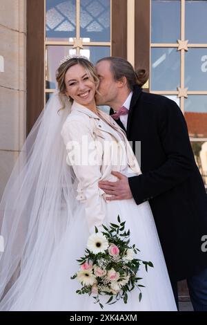 Le marié embrasse doucement la mariée sur le cou, la mariée regarde la caméra et rit joyeusement Алекс целует Banque D'Images