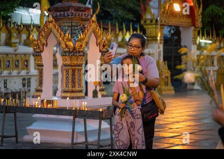 Bangkok, Thaïlande. 20 juillet 2024. Mère et fille sont vues prendre un selfie avec leurs offrandes, lors de la cérémonie de la Journée Asalha Puja au temple Wat Thepleela. Aussi connu sous le nom de jour du Dharma, Asalha Puja est l'un des festivals les plus importants du bouddhisme Theravada, célébrant le premier sermon de Bouddha. La journée est considérée comme une occasion pour les bouddhistes de montrer leur gratitude en faisant des offrandes aux temples et en écoutant des sermons. Crédit : SOPA images Limited/Alamy Live News Banque D'Images