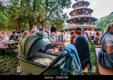 Kocherlball am Chinesischen Turm, Brotzeit und Biertrinken im Morgengrauen um 5:20 Uhr, München, 21. Juillet 2024 Deutschland, München, 21. Juillet 2024, Biertrinken BEI Kerzenschein um 5:20 Uhr, Kocherlball am Chinesischen Turm, Englischer Garten, Baby schläft selig im Kinderwagen, während die Eltern sich traditionell eine Brotzeit mit Bier gönnen, feiern Früh morgens, halb in der Nacht, tragen Tracht, tradition entstand im 19. Jahrhundert, als HausPersonal, Dienstboten und KöchInnen in den frühen Morgenstunden vor Dienstbeginn gefeiert und getanzt haben, tradition wurde ab 1989 wiederbelebt, tradi Banque D'Images