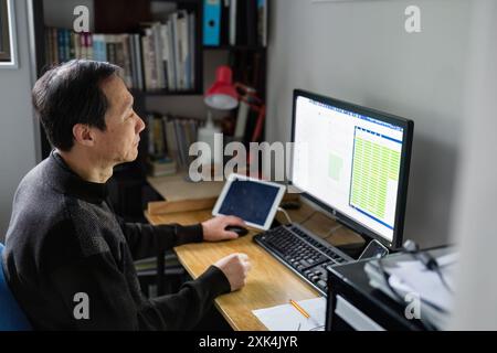 Homme travaillant sur ordinateur portable à la maison, graphiques à barres s'affichant sur l'écran de l'ordinateur. Banque D'Images