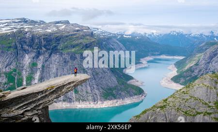 Un randonneur solitaire se dresse au bord de la falaise de Trolltunga en Norvège, surplombant un vaste fjord bleu. Femmes asiatiques à Trolltunga, Norvège Banque D'Images