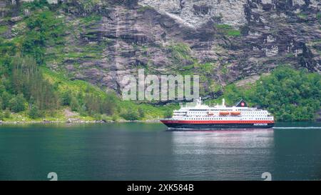 Geiranger Fjord Norvège 5 juillet 2024, Un bateau de croisière glisse dans les eaux sereines d'un fjord norvégien, avec d'imposantes falaises et une végétation luxuriante encadrant la scène. Banque D'Images