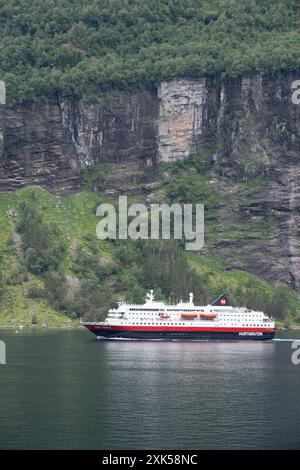 Geiranger Fjord Norvège 5 juillet 2024, Un bateau de croisière navigue à travers un fjord étroit et pittoresque, entouré de falaises verdoyantes couvertes de verdure luxuriante. Banque D'Images