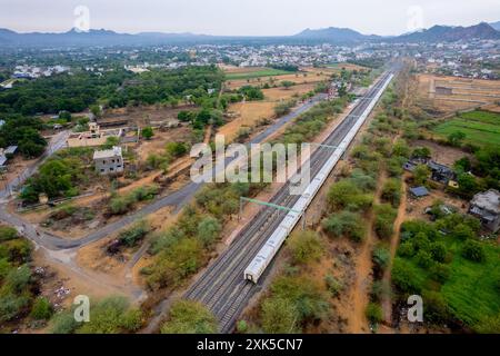 prise de vue aérienne par drone montrant un train debout sur une voie ferrée au milieu de champs verdoyants, les montagnes d'aravalli sur une petite gare montrant le chemin de fer Banque D'Images