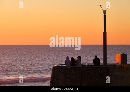 Les gens regardant le coucher de soleil dans la lumière dorée depuis un belvédère d'observation en bord de mer avec un espace de copie à Scarborough Beach, Perth, Australie occidentale. Banque D'Images