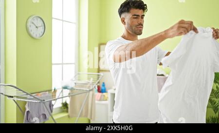 Beau jeune homme hispanique pliant le linge à l'intérieur dans une pièce verte lumineuse. Banque D'Images