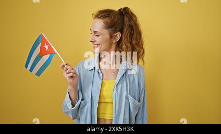 Femme caucasienne souriante tenant un drapeau cubain sur un fond jaune isolé. Banque D'Images