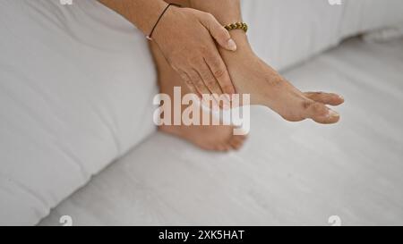 Un homme se relaxant pieds nus dans une chambre simple avec literie blanche, mettant en valeur le confort décontracté et la tranquillité à la maison. Banque D'Images