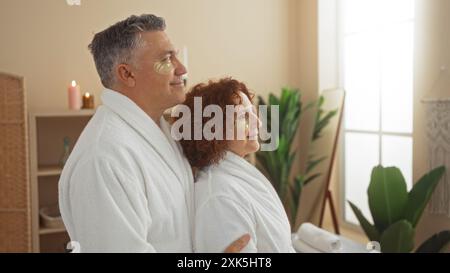 Couple d'âge moyen profitant d'un moment serein avec des masques pour les yeux dans une salle de spa paisible, ornée de verdure et de bougies, mettant en valeur la détente, la beauté, un Banque D'Images