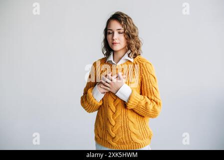 Jeune femme reconnaissante : exprimer le bonheur et la reconnaissance - mains sur la poitrine, équilibre mental - gentillesse, amour et gratitude - Portrait isolé sur Banque D'Images