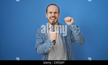 Homme chauve chante joyeusement tenant une brosse à cheveux comme un microphone sur un fond bleu Uni. Banque D'Images