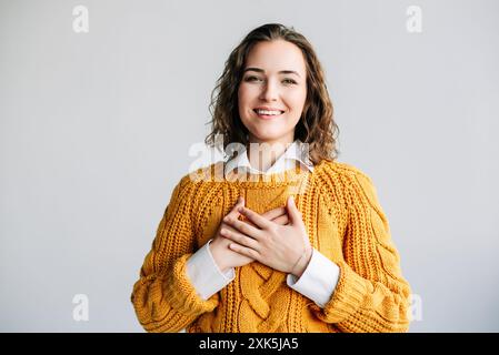 Reconnaissante jeune femme exprimant la gentillesse. Une jeune femme heureuse avec les mains sur la poitrine, montrant gratitude et gentillesse. fond blanc, rayonnant Banque D'Images