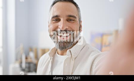 Un homme hispanique senior joyeux avec une barbe et des cheveux gris souriant dans un cadre de studio intérieur lumineux. Banque D'Images