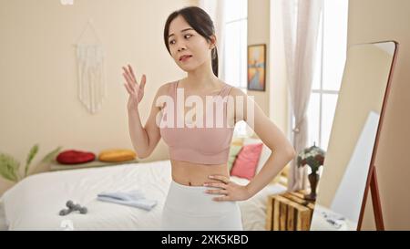 Une jeune femme asiatique prend une pose décontractée dans sa chambre élégante avec lumière naturelle et décor contemporain. Banque D'Images