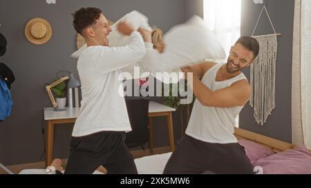 Deux hommes s'engageant ludique dans un combat d'oreiller sur le lit dans un cadre confortable de chambre soulignant leur amour et lien en tant que couple gay Banque D'Images