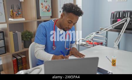 Jeune homme afro-américain dans une clinique vétérinaire portant des gommages, écrivant des notes à un bureau avec des livres médicaux et du matériel. Banque D'Images