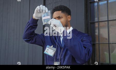 Un homme afro-américain concentré dans l'application de la loi examinant des preuves tout en se tenant debout dans une rue urbaine. Banque D'Images