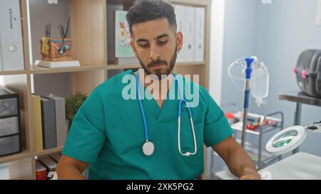 Bel homme hispanique dans des gommages verts avec un stéthoscope travaillant à l'intérieur dans une clinique vétérinaire. Banque D'Images