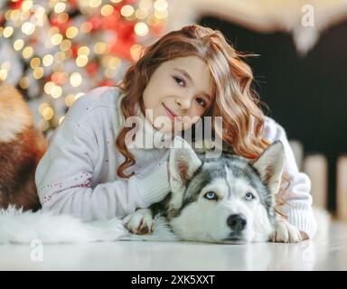 Gros plan de fille mignonne embrassant chien Husky sur fond de noël Banque D'Images