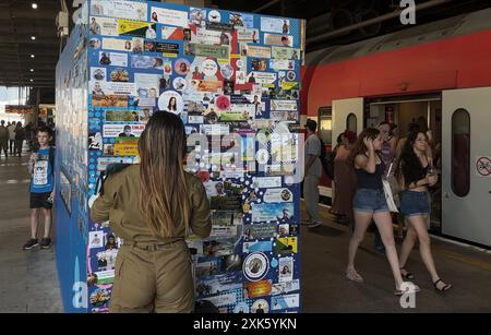 TEL AVIV, ISRAËL- 21 JUILLET : une soldat israélienne se tient à côté d'un mur avec des autocollants commémoratifs commémorant les soldats de Tsahal tués dans la guerre israélienne contre Gaza et ter­ror vic­tims après Octo­ber 7, dans la gare de Hashalom, au milieu des batailles continues entre Israël et le groupe militant Hamas à Gaza le 21 juillet 2024 à tel Aviv. Israël. Banque D'Images