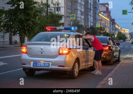 Officier de police parlant à l'automobiliste dans la rue de la ville au crépuscule, avec les feux de voitures de patrouille clignotants en arrière-plan Banque D'Images