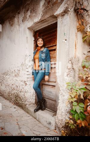 Une femme portant une veste en denim et un Jean se penche contre une porte, regardant à gauche du cadre. Banque D'Images