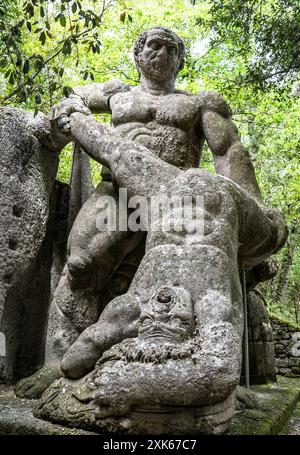 Ancienne sculpture en pierre peperino représentant le mythe d'Hercule et Cacus ou Hercule et Lyca. La statue, couverte de mousse, est entourée de gre luxuriant Banque D'Images