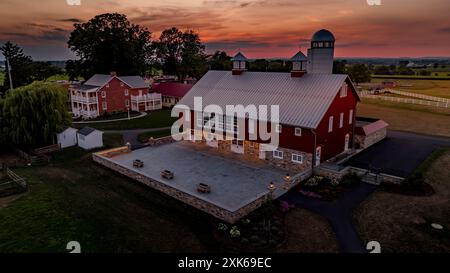 Ronks, Pennsylvanie, États-Unis, 19 juillet 2024 - Tranquil Farm Scene at Sunset dispose D'Une grande grange rouge avec Une fondation en pierre, Une cour en pierre spacieuse, Une maison en brique à proximité, et Un ciel coloré, créant Un cadre paisible et pittoresque. Banque D'Images